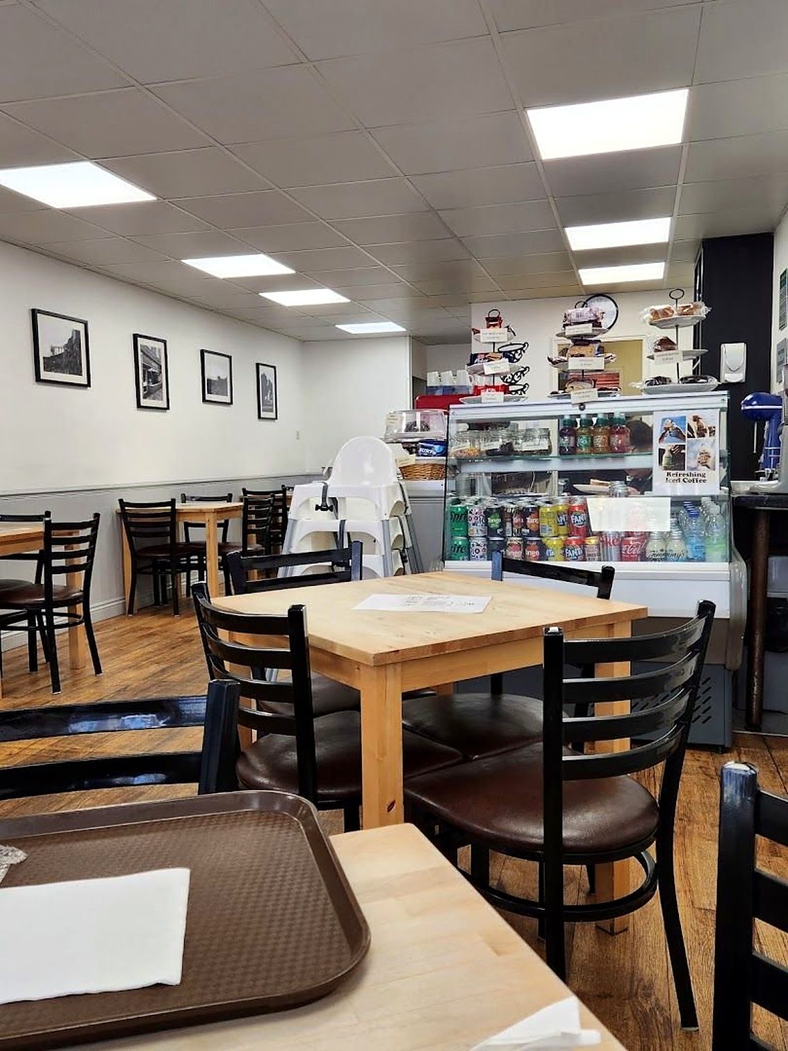 Inside Cafe Fusion: light wooden tables, black chairs, framed pictures on white walls and a drinks fridge at the back